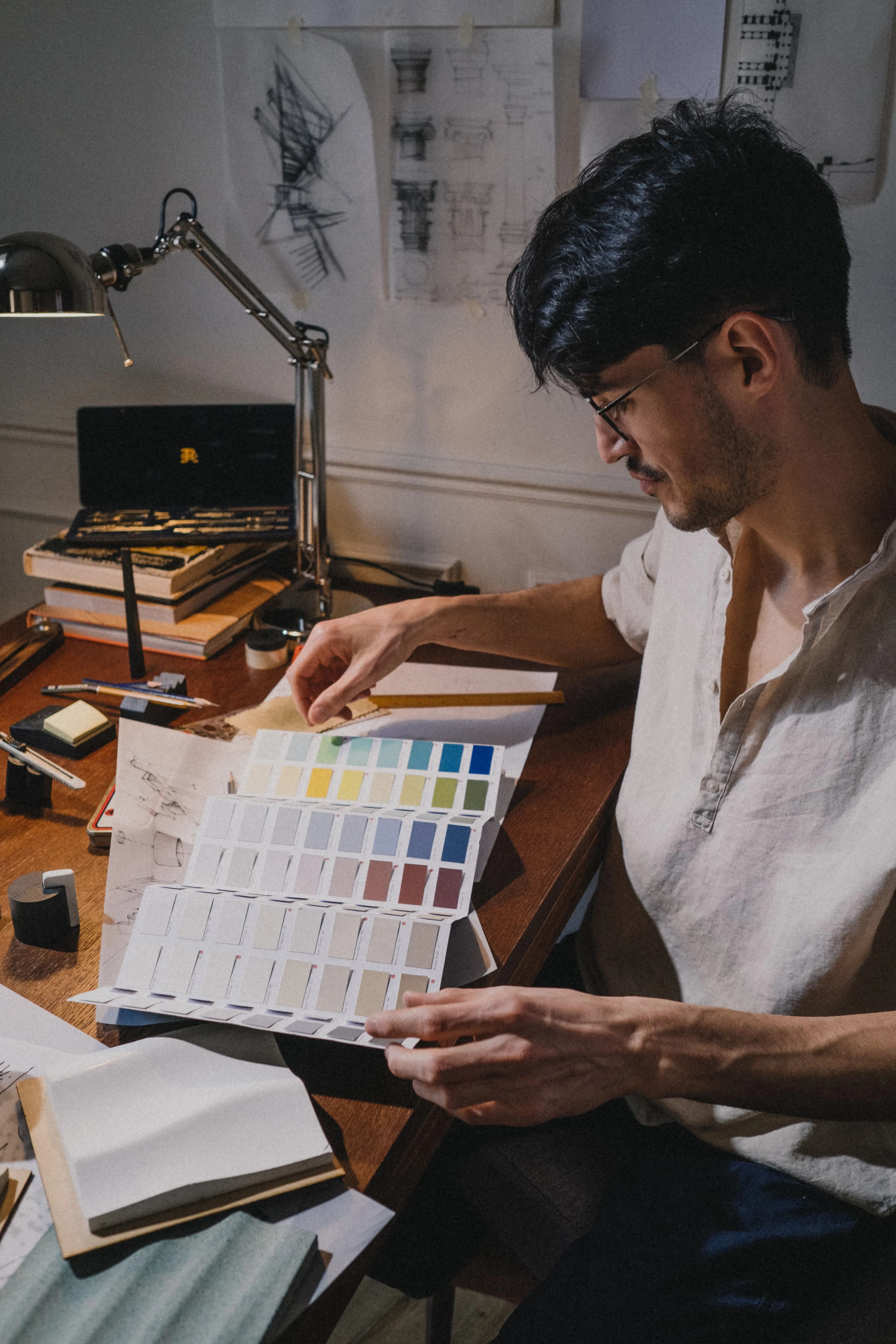 A designer at a lamplit desk comparing colour swatches beside pinned sketches
